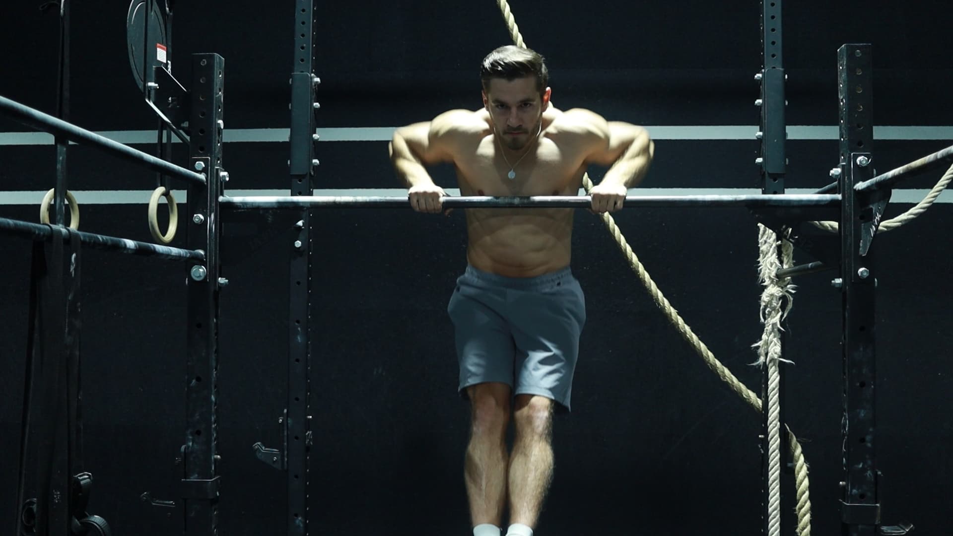 Male athlete pressing above a pull-up bar in a bar muscle up, arms near full extension, in a minimalist industrial gym