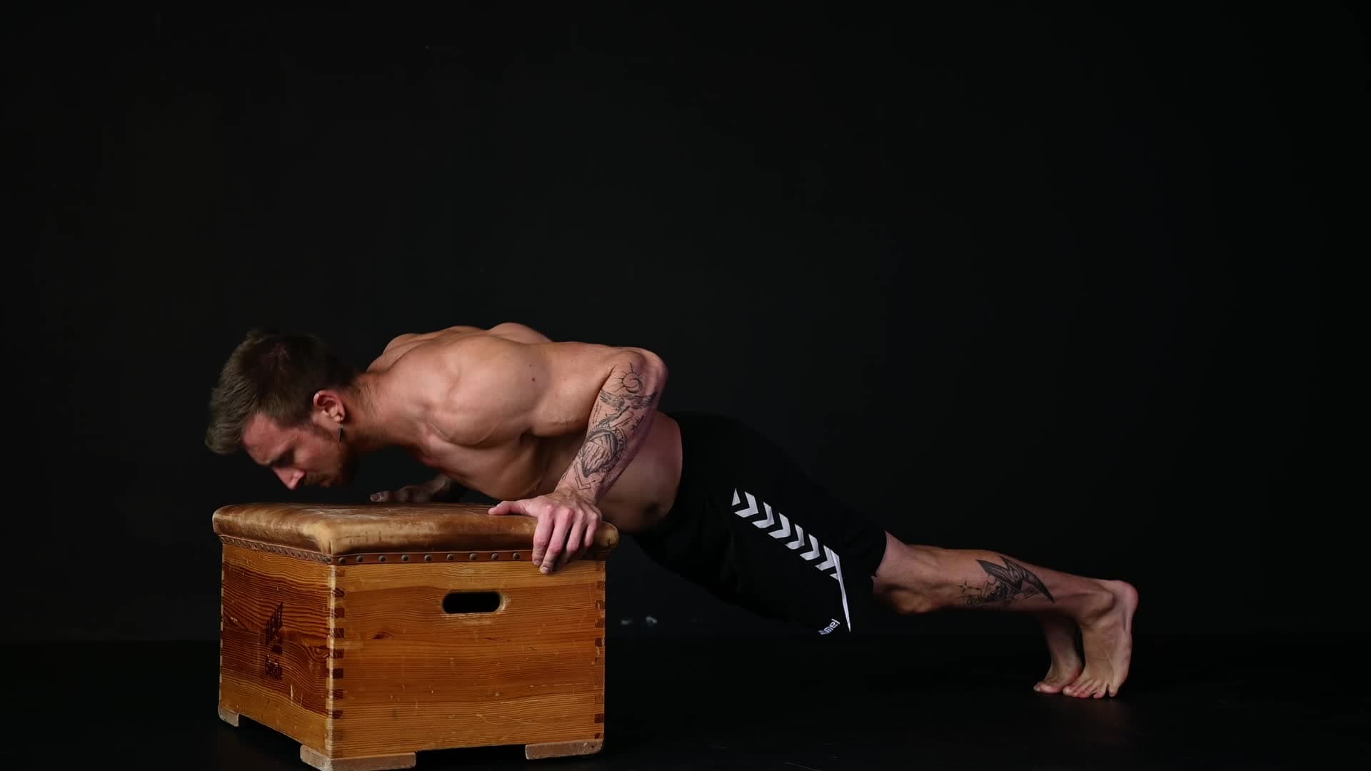 Male athlete performing a perfect incline push-up in a minimalist gym with concrete wall and black rubber floor mats
