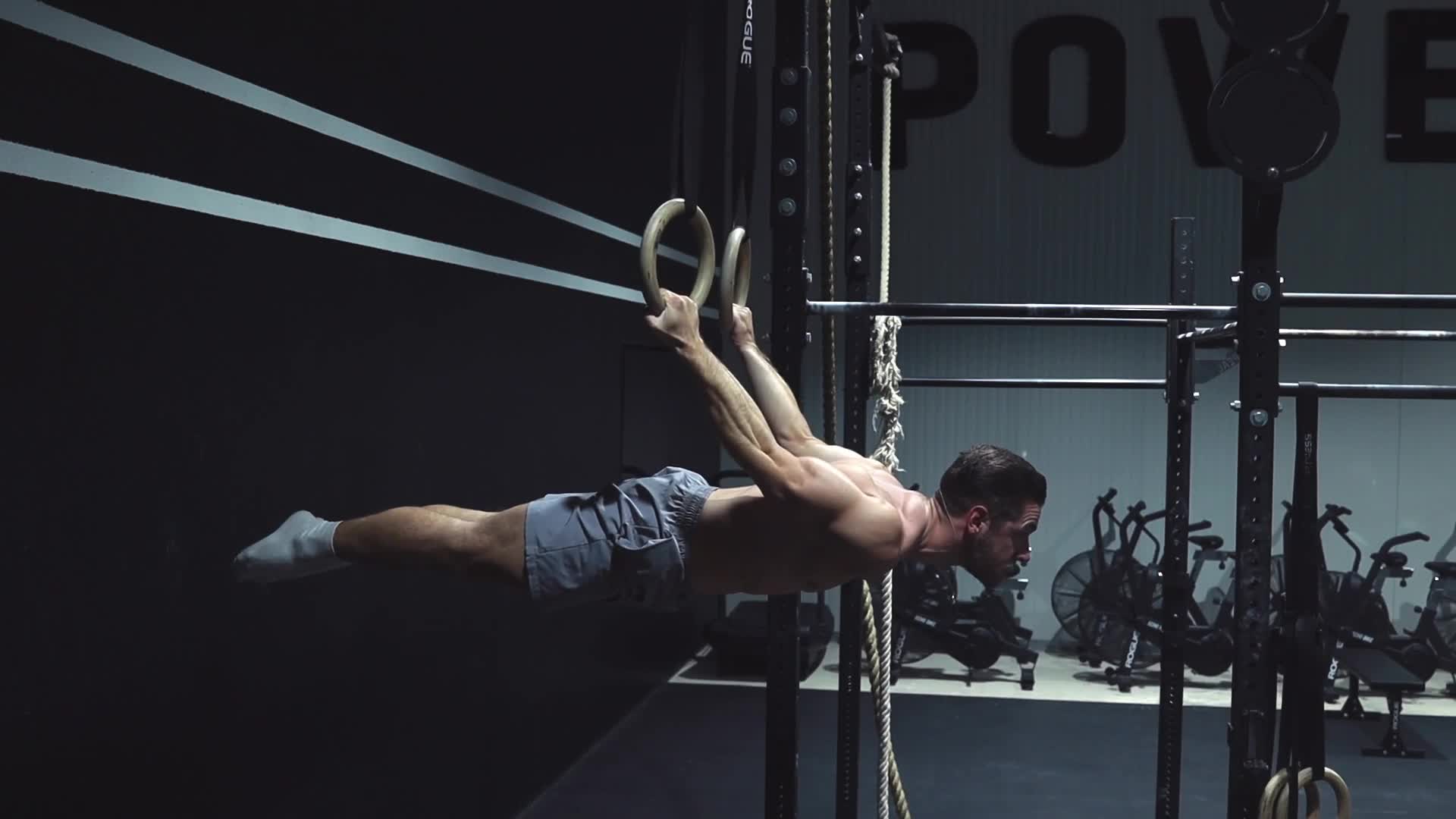 Athlète réalisant un back lever complet sur des anneaux de gymnastique dans une salle minimaliste