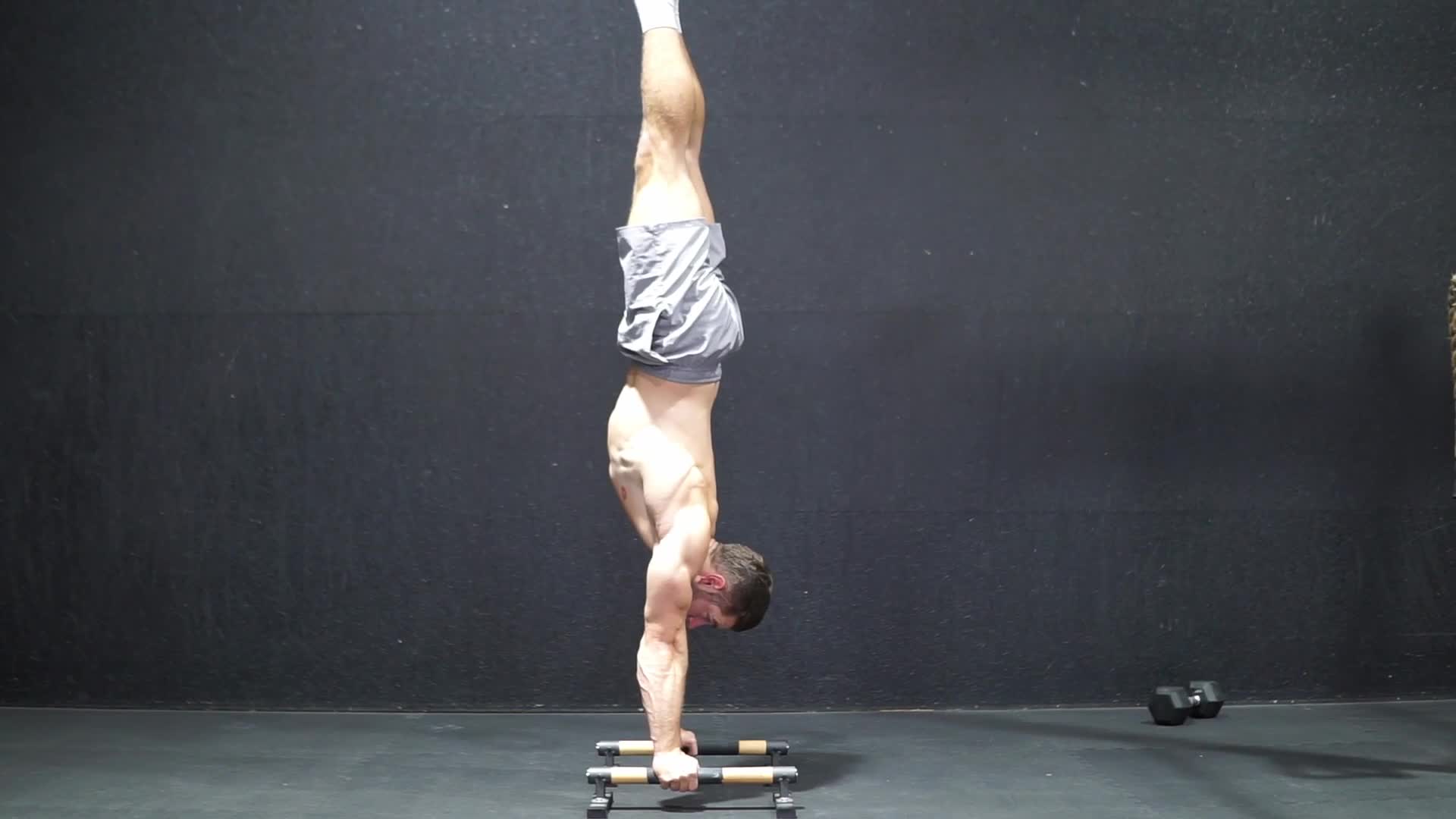 Male athlete holding a freestanding handstand with perfect vertical alignment on black rubber mats in a minimalist industrial gym